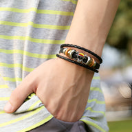 Bracelet multi-rangs en cuir noir avec perles métalliques et cordons tressés porté au poignet homme.
