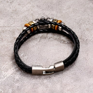 Bracelet multi-rangs en cuir noir tressé avec fermoir métallique argenté et perles décoratives en bois et métal.