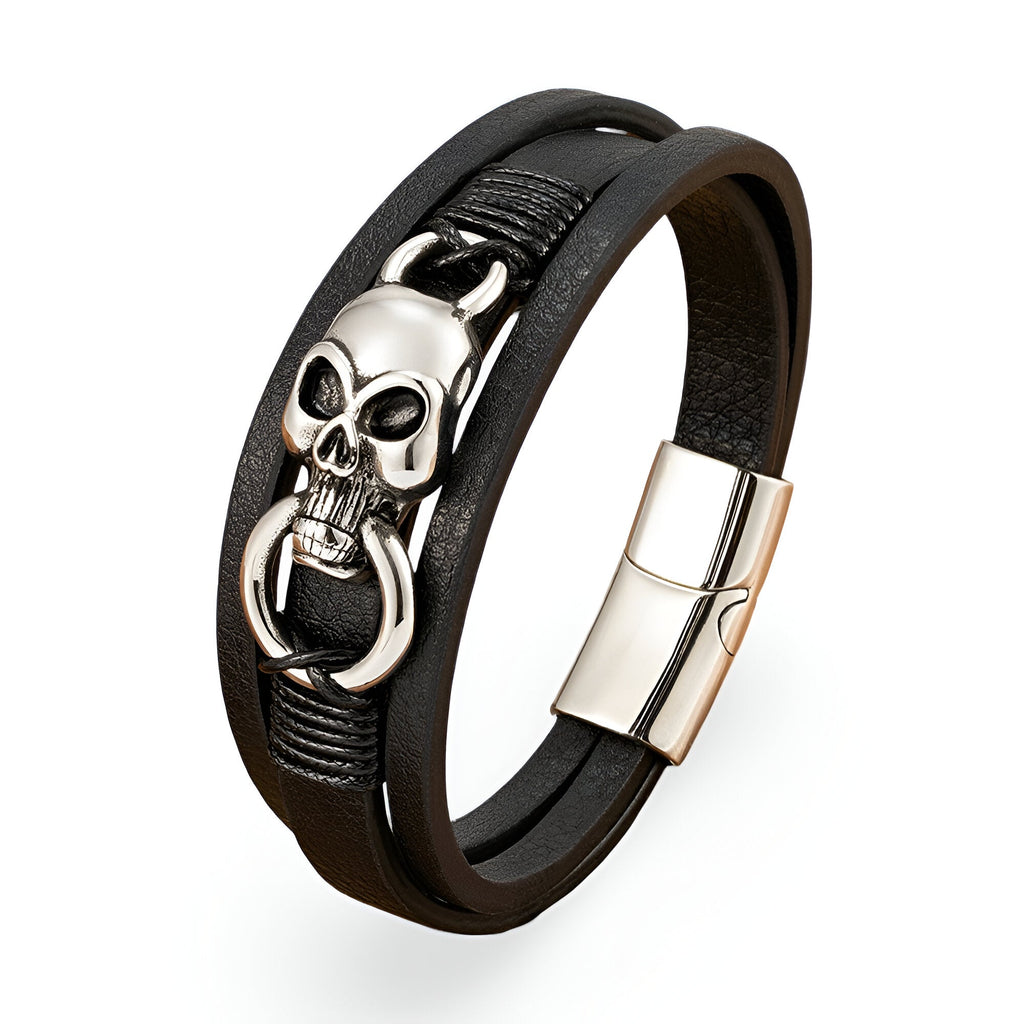 Bracelet multi-rangs en cuir noir avec tête de mort argentée et anneau, fermoir métallique brillant.