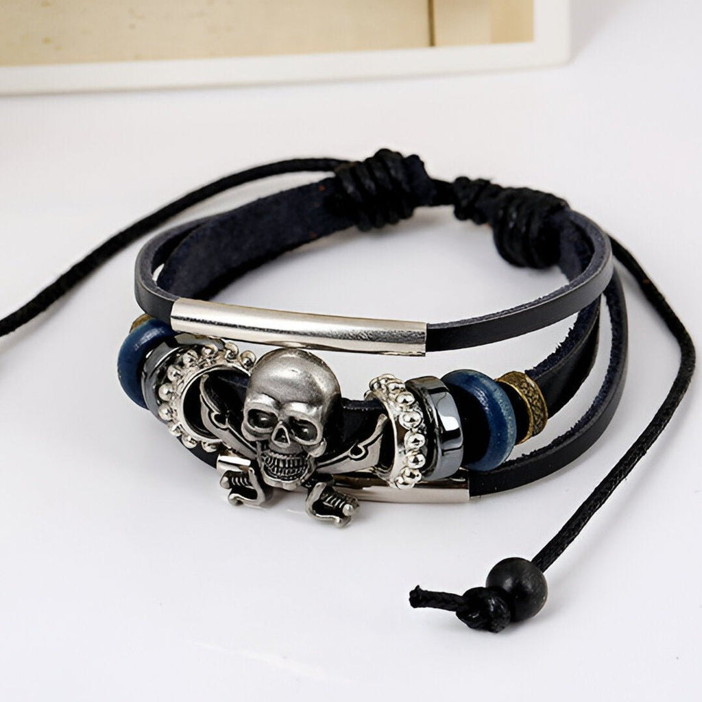 Bracelet multi-rangs en cuir noir avec tête de mort pirate en métal argenté et détails bleus et argentés.