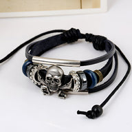 Bracelet multi-rangs en cuir noir avec tête de mort pirate en métal argenté et détails bleus et argentés.