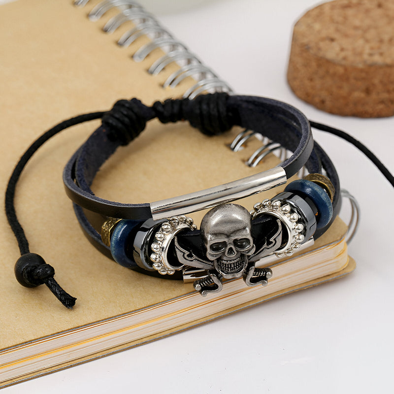 Bracelet multi-rangs en cuir noir avec tête de mort pirate en métal argenté et perles bleues et noires.