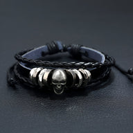 Bracelet multi-rangs en cuir noir avec tête de mort argentée et anneaux métalliques.