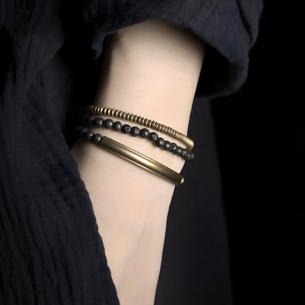 Bracelet multi-rangs en cuivre doré avec perles noires mates en pierres volcaniques sur poignet féminin.