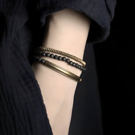 Bracelet multi-rangs en cuivre doré avec perles noires mates en pierres volcaniques sur poignet féminin.