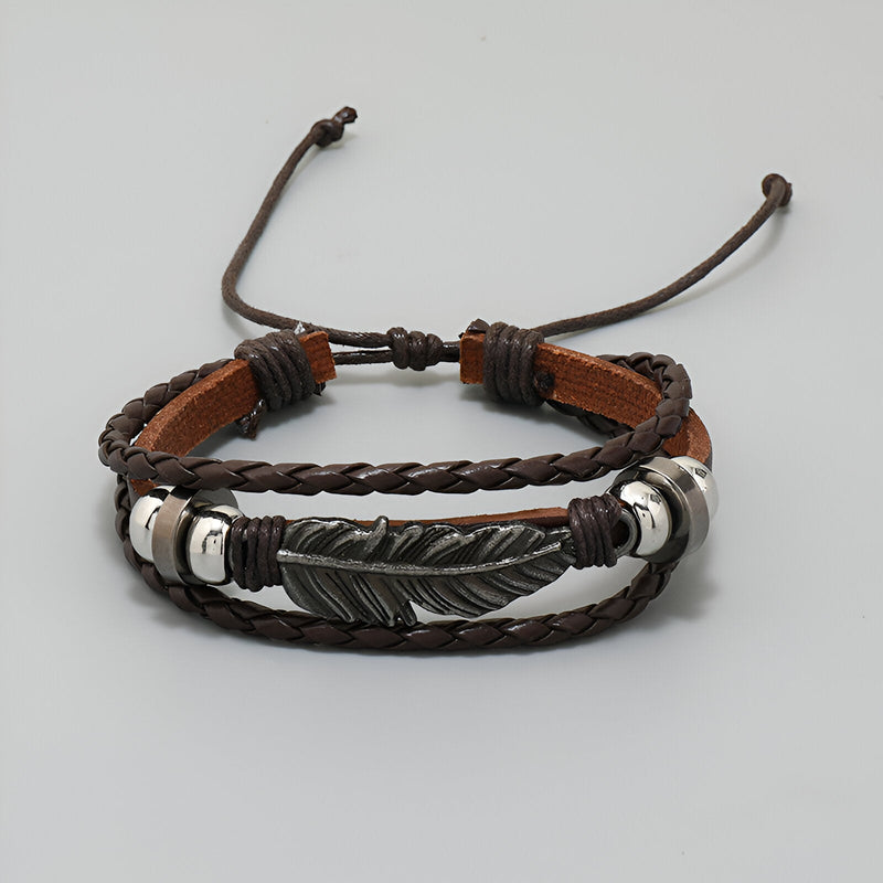 Bracelet multi-rangs marron en microfibre avec grande plume métallique gravée et cordons ajustables.