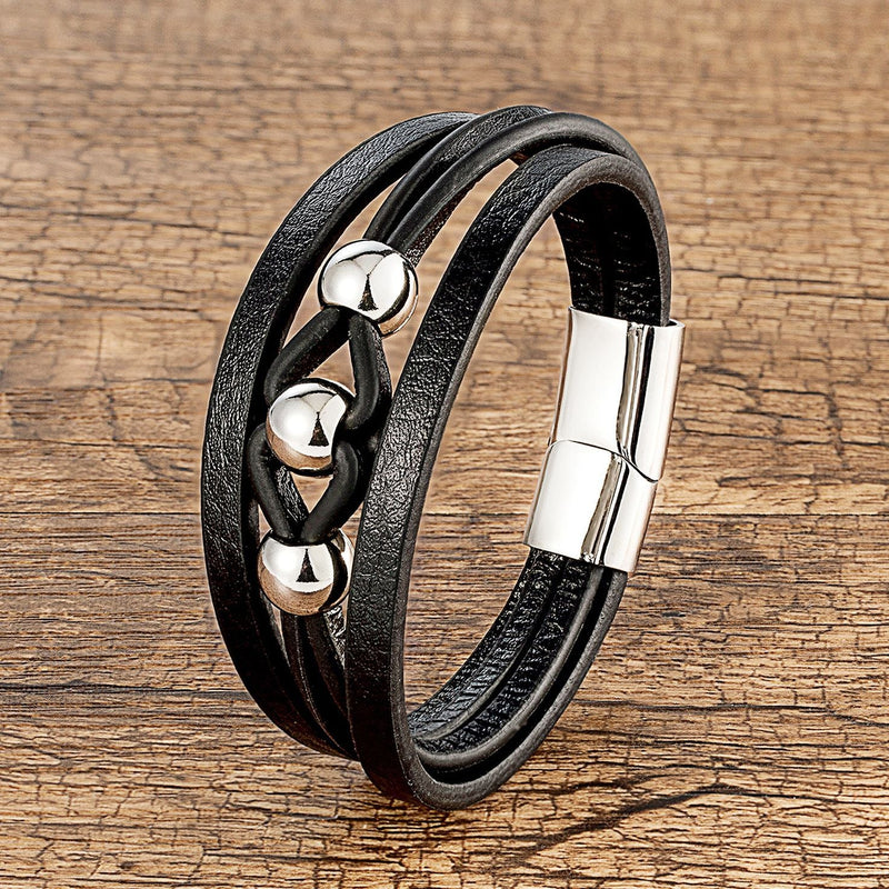 Bracelet multi-rangs en microfibre noire avec breloques métalliques argentées et fermoir magnétique.