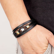 Bracelet multi-rangs en microfibre noire avec breloques métalliques dorées sur poignet homme.