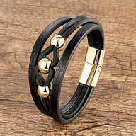 Bracelet multi-rangs en microfibre noire avec breloques métalliques dorées et fermoir magnétique doré.