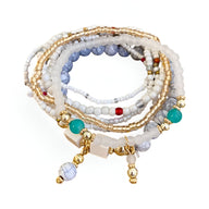 Bracelet multi-rangs élastique perles blanches, bleues et dorées avec charms pendants turquoise et doré.