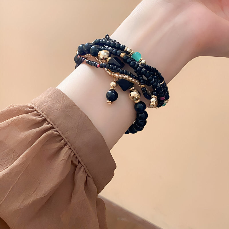 Bracelet multi-rangs élastique en perles noires et dorées avec détails turquoise et charmes suspendus.