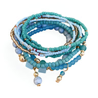 Bracelet multi-rangs élastique en perles turquoise et bleues avec petits pendentifs dorés.