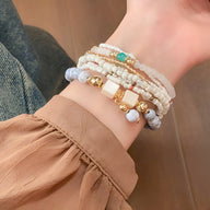 Bracelet multi-rangs élastique avec perles blanches, dorées et turquoise, style bohème chic.