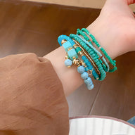 Bracelet multi-rangs bleu et turquoise en perles de résine avec petits charms dorés sur poignet féminin.