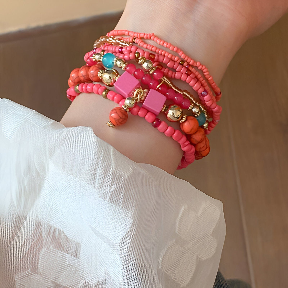 Bracelet multi-rangs en perles de résine roses et corail avec détails dorés sur poignet femme.