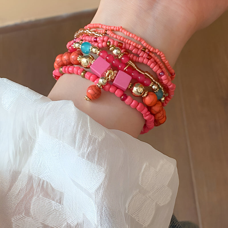 Bracelet multi-rangs en perles de résine roses et corail avec détails dorés sur poignet femme.