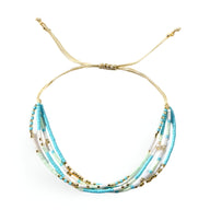 Bracelet multi-rangs en perles heishi bleu clair et turquoise avec perles dorées et cordon beige ajustable.
