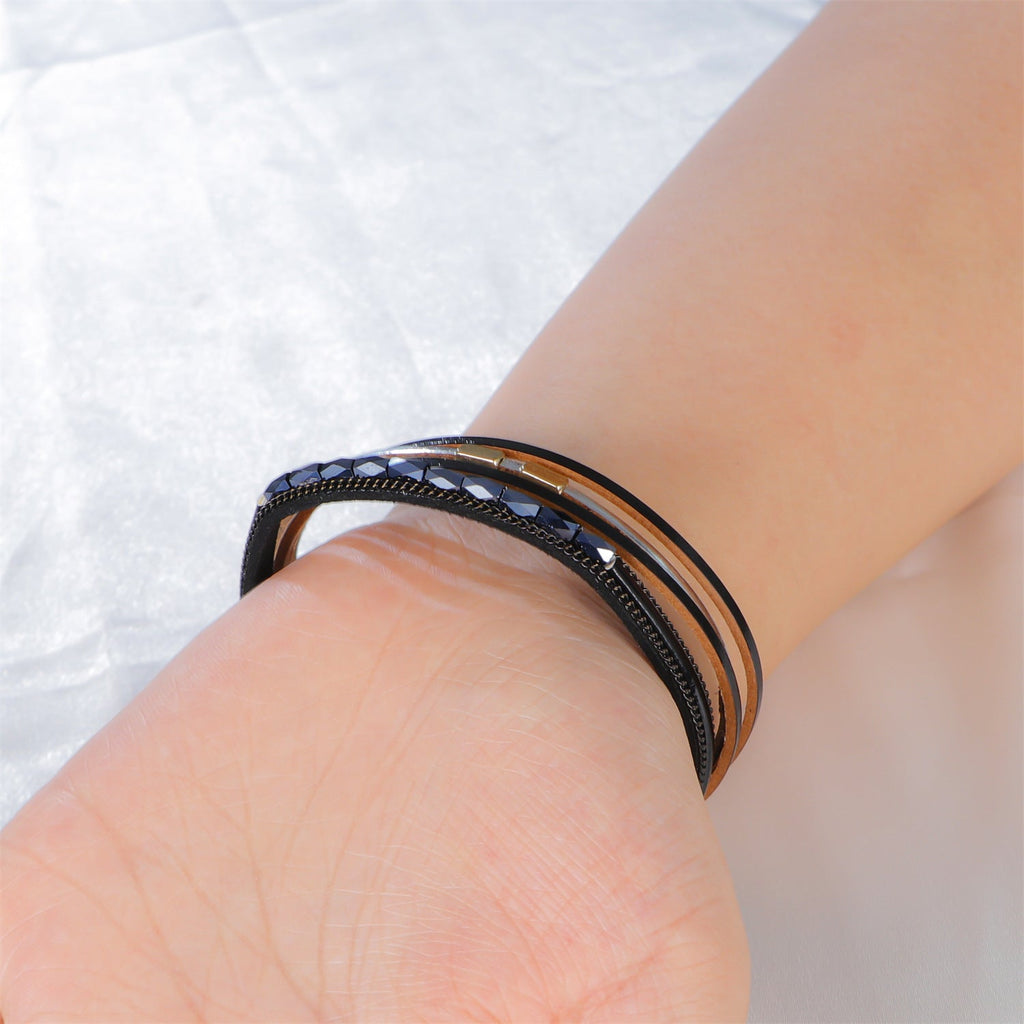 Bracelet multi-rangs noir avec détails métalliques brillants au style bohème sur poignet clair.