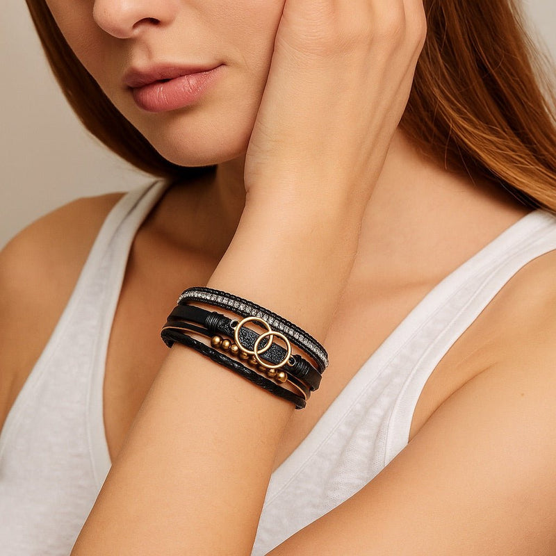 Bracelet multi-rangs noir en simili cuir avec strass et anneaux dorés, fermoir magnétique chic.