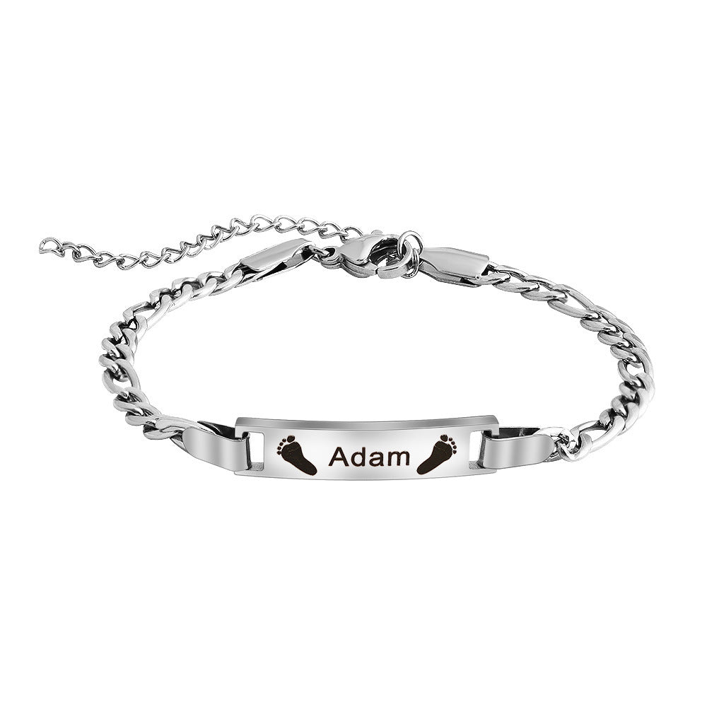 Bracelet naissance en acier argenté avec maille gourmette fine et plaque gravée prénom Adam et petits pieds noirs.