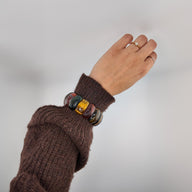 Bracelet en pierres naturelles d'œil de tigre aux reflets jaunes et bruns, design rond et lisse, porté au poignet.