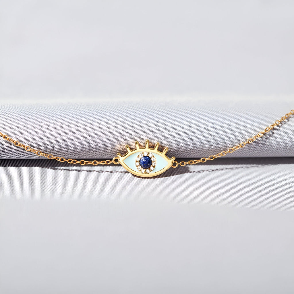 Bracelet femme en or avec pendentif œil serti d'une pierre bleue centrale et détails cloutés sur la paupière.