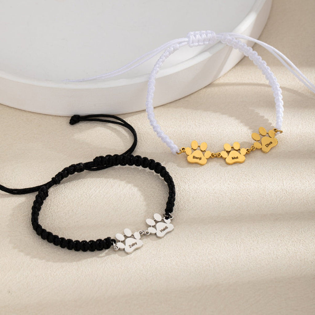 Bracelet nylon noir avec trois pattes en acier inoxydable argenté et bracelet nylon blanc avec trois pattes dorées.