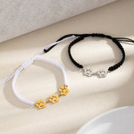 Bracelet en nylon tressé blanc avec pampilles patte dorées et bracelet noir avec pampilles patte argentées.