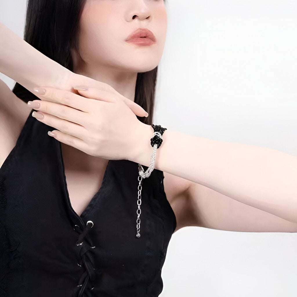 Bracelet perlé noir avec nœud central ajustable en chaîne argentée porté au poignet féminin.