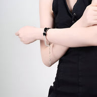 Bracelet perlé noir avec nœud central et chaîne argentée porté sur poignet féminin.