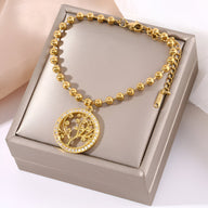 Bracelet perlé en titane doré avec pendentif arbre de vie cerclé de cristaux blancs.