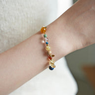 Bracelet perlé avec pierres naturelles multicolores et éclats dorés sur poignet, design élégant et fin.