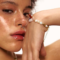 Bracelet à perles baroques blanches et pierres naturelles multicolores avec fermoir doré fin sur poignet féminin.