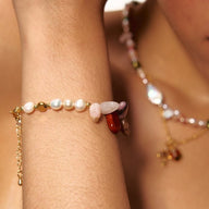 Bracelet doré avec perles baroques blanches et pierres naturelles multicolores sur peau féminine.