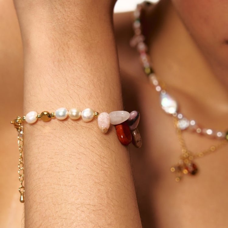 Bracelet doré avec perles baroques blanches et pierres naturelles multicolores sur peau féminine.