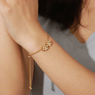 Bracelet fin en acier inoxydable or avec pendentifs hexagonaux délicats porté au poignet.