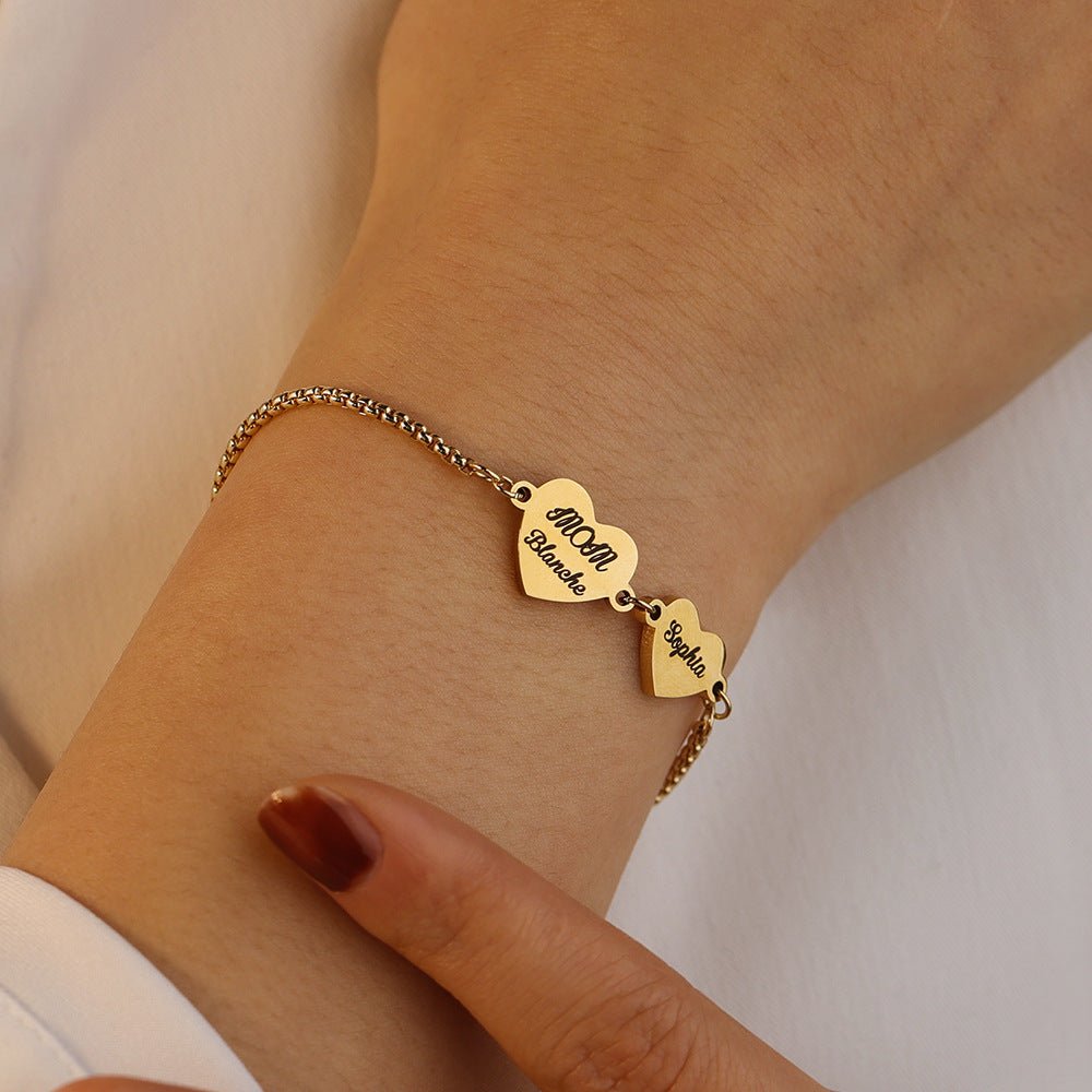 Bracelet en acier inoxydable doré avec deux cœurs gravés, chaîne fine ajustable, porté au poignet.