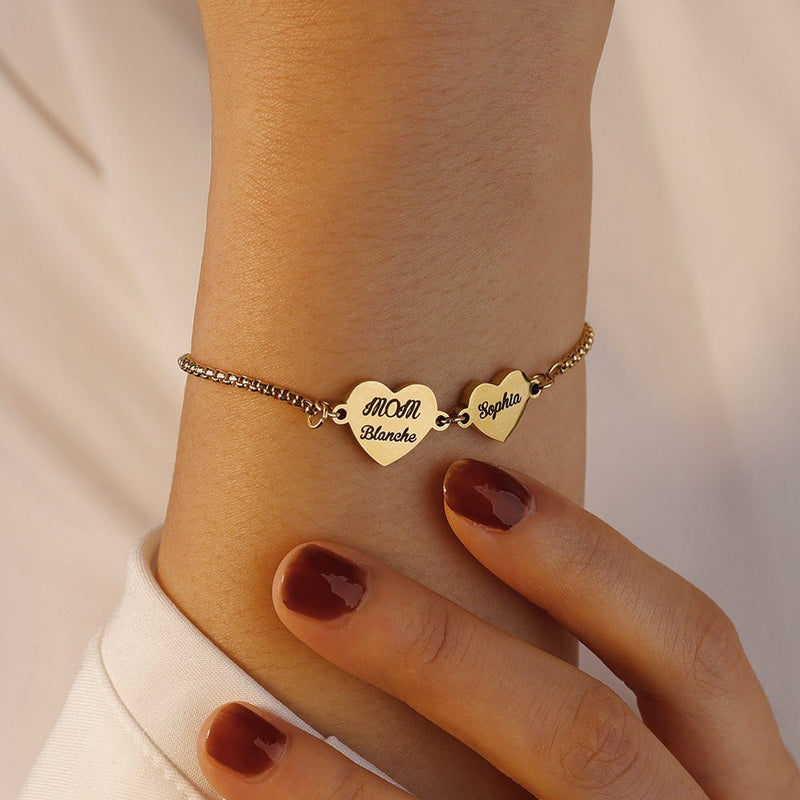 Bracelet fin en acier inoxydable avec trois cœurs gravés de prénoms, chaîne ajustable argentée.