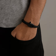 Bracelet noir à mousqueton en corde tressée porté au poignet d’homme, style minimaliste.
