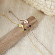Trois bracelets fins en acier inoxydable or et rose, avec pendentifs cœur gravés et un motif noir rond sur chaîne délicate.