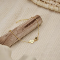 Bracelet fin en acier inoxydable doré avec pendentif cœur gravé et petit médaillon rond, style délicat et élégant.