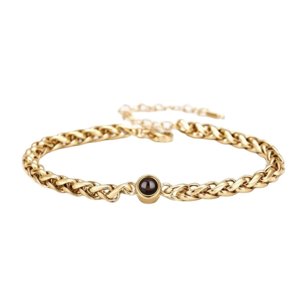 Bracelet fin en maille tressée en acier inoxydable doré avec perle noire centrale et fermoir réglable.