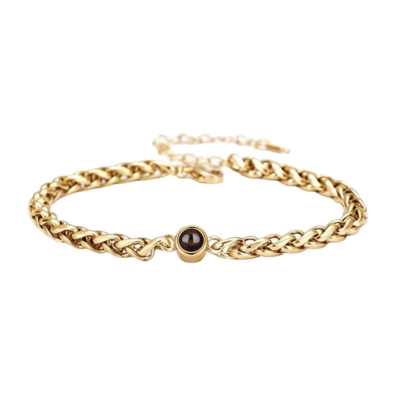 Bracelet fin en maille tressée en acier inoxydable doré avec perle noire centrale et fermoir réglable.