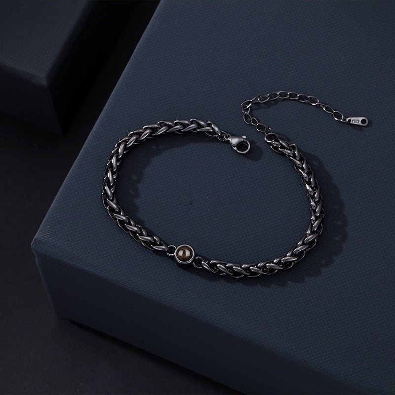 Bracelet en acier inoxydable noir tressé avec une médaille ronde centrale et fermoir réglable.