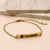 Bracelet gourmette ajustable en métal doré avec un pendentif rectangulaire gravé d’un code Spotify noir.