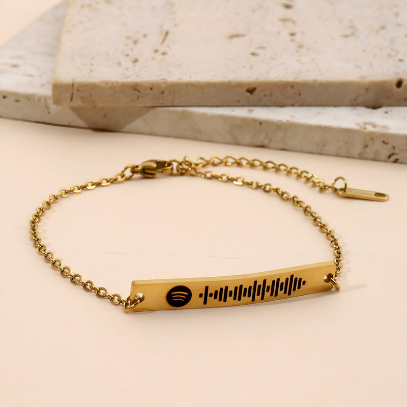 Bracelet gourmette ajustable en métal doré avec un pendentif rectangulaire gravé d’un code Spotify noir.