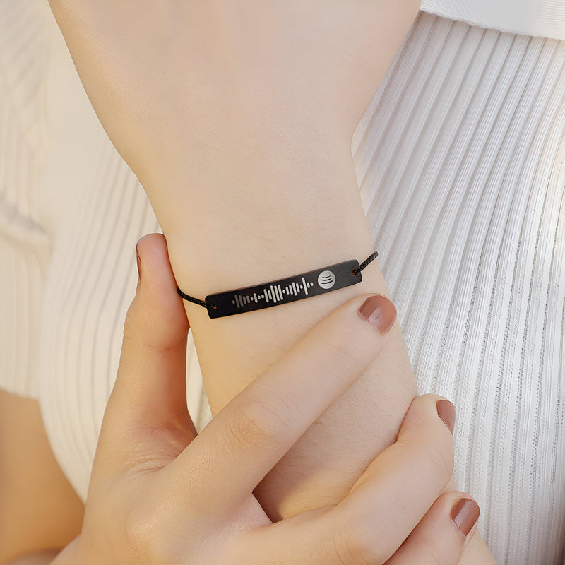 Bracelet gourmette noir ajustable avec code Spotify gravé et bouton blanc sur poignet féminin.