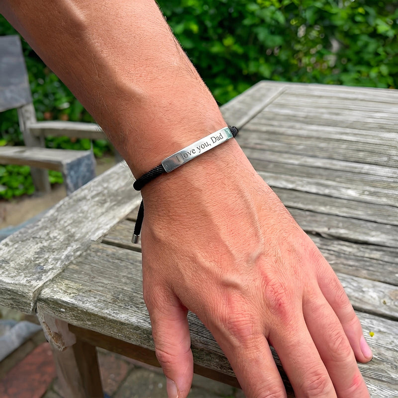 Bracelet cordon noir avec barre en acier inoxydable gravée, fermoir coulissant ajustable, style minimaliste.