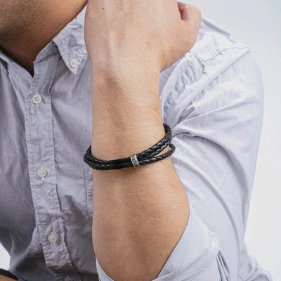 Bracelet en cuir noir triple tour avec anneau métallique gravable, porté au poignet.