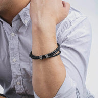 Bracelet cuir noir triple tour avec deux anneaux gravés porté au poignet homme.
